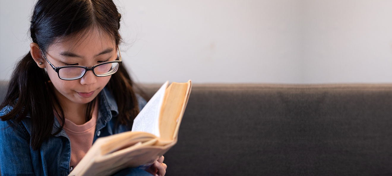 Asian Teenage Girl Reading Book And Sitting On Couch At Home